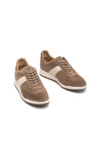 Sneaker in suede marrone con una striscia in pelle bianca, punta rotonda, design con lacci e interno beige. Suola testurizzata per una buona aderenza.