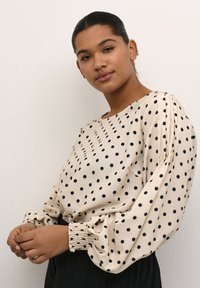 Krämfärgad blus med svarta prickar, lös passform och samlade ärmar. Slät tygkvalitet med lätt struktur. Minimalistisk design, rund halsringning.