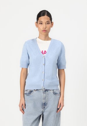 Lichtblauwe, korte mouwen cardigan met bloemenbreipatroon, v-hals en knoopsluiting. G gedragen over een wit t-shirt en losse denim jeans.