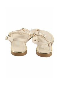 Sandales beiges avec un accent doré, présentant une lanière tressée ornée de perles blanches. Semelle plate avec une texture lisse. Fermeture à boucle.