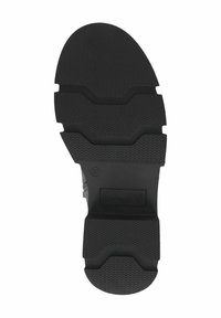 Suela de zapato de goma negra, con un patrón de banda de rodadura que presenta surcos en zigzag y bordes redondeados. Nombre de la marca "CAPRICE" grabado en la parte inferior.
