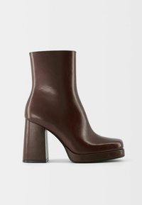 Bottine en cuir marron foncé avec bout carré et talon épais à bloc sur fond gris clair.