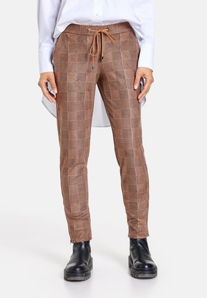 Pantaloni a quadri marroni con vita a laccio, gamba affusolata e polsini con cerniera, abbinati a stivaletti neri alla caviglia. Tessuto dalla texture liscia.