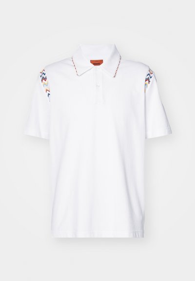 Baltas polo krekls, kas izgatavots no kokvilnas, ar krāsainu zigzaga izšuvumu uz piedurknēm un pogātu apkakli ar zīmola birku.