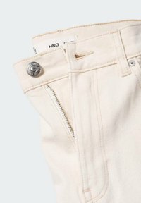Détail d’un pantalon en denim blanc cassé montrant la taille, un bouton métal, une poche zippée, une passants pour ceinture et une étiquette partielle de la marque « MNG ».
