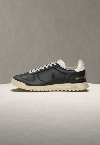 Μαύρο και μπεζ χαμηλό sneaker με άσπρα κορδόνια, λογότυπο Polo στο πλάι και υπογραφή «Ralph Lauren» σε χρυσό κοντά στη φτέρνα.