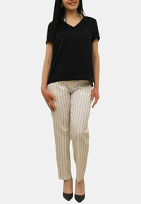 Top nero a maniche corte con scollo a V, abbinato a pantaloni bianchi a righe. I pantaloni presentano righe verticali blu navy. La modella indossa tacchi neri e si trova di fronte.