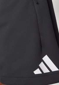Svarta atletiska shorts i slätt tyg med en vit Adidas-logotyp i tre diagonala ränder i det nedre högra hörnet.
