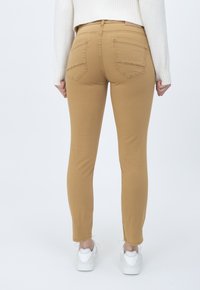 Pantalones khaki ajustados con una textura suave, cinco bolsillos y parche con logo en la cintura trasera. Combinados con zapatillas blancas.