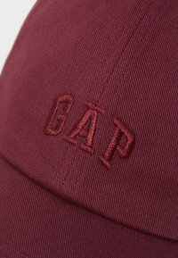 Mørkerød bomuldskeps med broderet "GAP" logo. Tekstureret stof og struktureret skygge med synlige syningsdetaljer.
