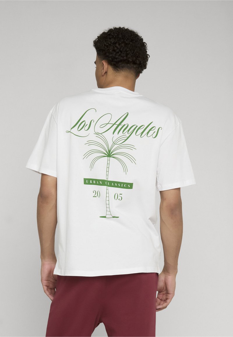 Homme vu de dos portant un t-shirt blanc avec un palmier vert et le texte « Los Angeles Urban Classics 2005 », associé à un pantalon rouge foncé.