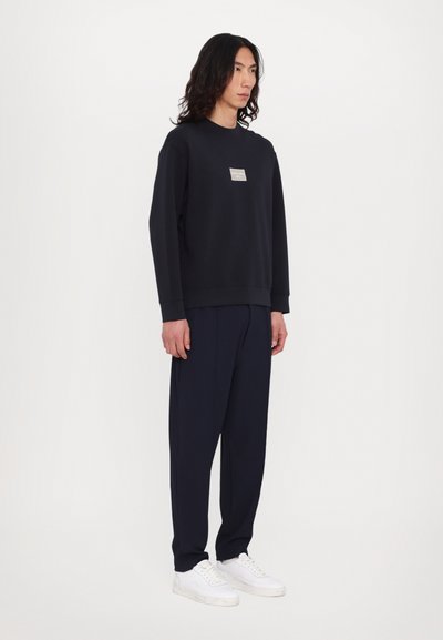 Sweat-shirt navy avec un col rond et un petit patch logo, associé à un pantalon navy assorti et des baskets blanches. Texture de tissu lisse.