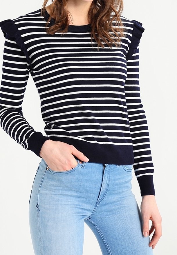 Pull à rayures bleu marine et blanches avec épaules volantées, col rond et poignets côtelés, associé à un jean en denim bleu clair.