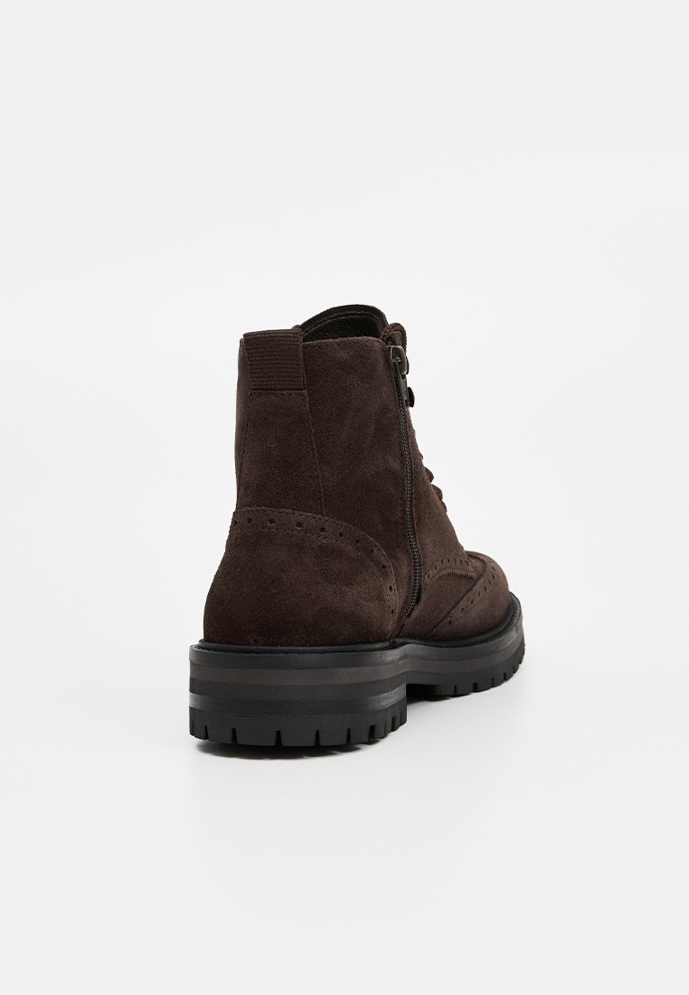 Braune Wildleder-Ankle-Boots mit flacher schwarzer Gummisohle, Schnürung an der Vorderseite und seitlichem Reißverschluss. Mit Brogue-Details entlang der Kanten.