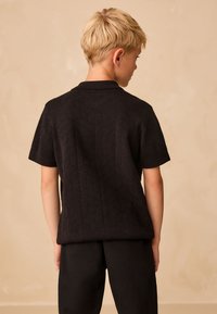 Czarna koszulka polo z krótkim rękawem, z teksturowanym geometrycznym wzorem. Tkanina jest gładka, z klasycznym kołnierzem i luźnym krojem.