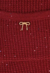 Roter gestrickter Pullover mit einem strukturierten Muster, verziert mit kleinen Pailletten und einem goldenen metallischen Schleifenakzent in der Mitte.