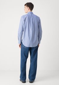 Niebiesko-biała bawełniana koszula w paski z długim rękawem i kołnierzykiem na guziki, zestawiona z luźnymi niebieskimi dżinsami i czarnymi butami.