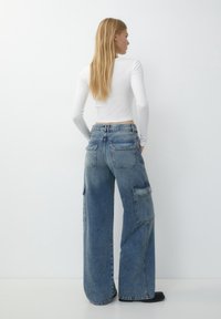 Högmidjade, vida denimjeans i ljusblått med subtil blekning, flera fickor och en avslappnad passform. Matchas med en åtsittande vit långärmad topp.