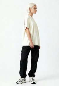 Krēmkrāsas pārmērīgs T-krekls ar īsām piedurknēm, apvienots ar brīvi piegulošiem melniem kravas biksēm un sportiskām baltām kedām.