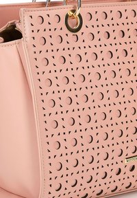 Roze synthetische handtas met een laser-gezaagd ontwerp met cirkel- en driehoekpatronen, gouden hardware-accenten en een textuurafwerking.
