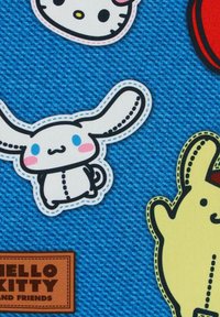 Fondo de tela azul con parches bordados: Hello Kitty, un conejo blanco con orejas grandes y un personaje amarillo, todos contorneados en negro.