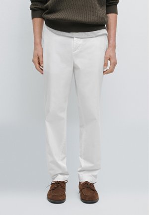 Pantalons en coton blancs à coupe droite, associés à des chaussures en suède marron. Portés avec un pull côtelé vert foncé et un t-shirt gris.