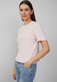 Hellrosa lässiges T-Shirt mit kurzen Ärmeln und Rundhalsausschnitt, aus Baumwolle gefertigt, mit einem lockeren Schnitt. Getragen mit verwaschenen blauen Jeans.