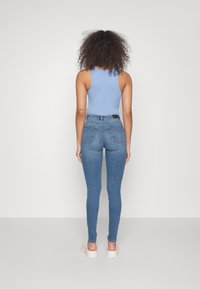Top azul sin mangas combinado con jeans ajustados de tiro medio en color azul, con bolsillos traseros y ligero desgaste, llevados con sandalias blancas gruesas.