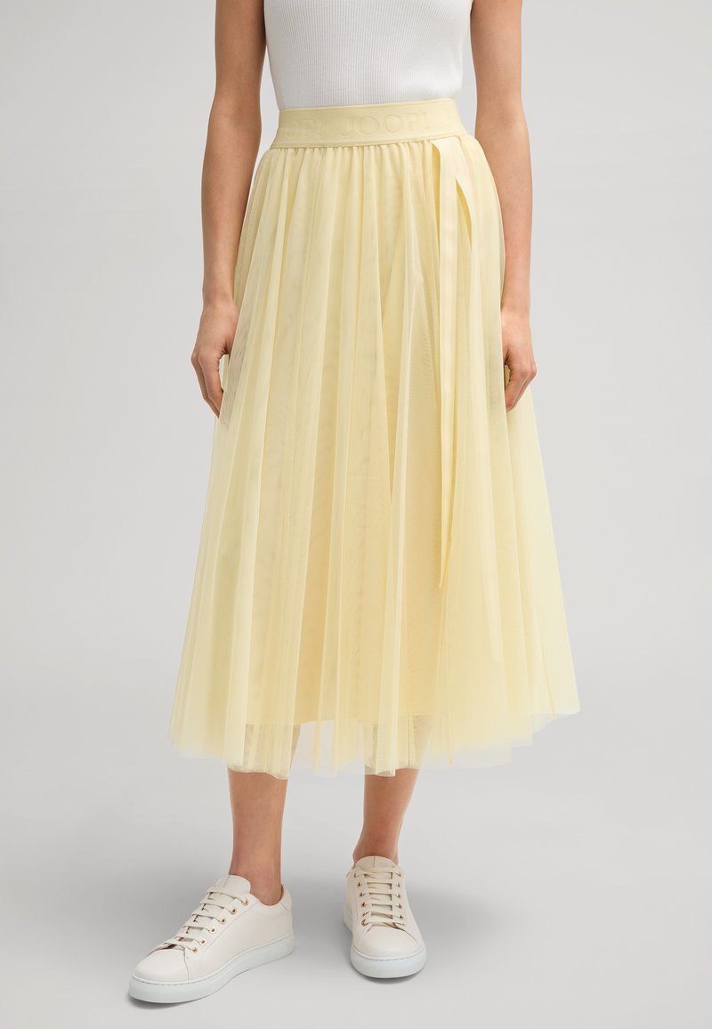 Gelber Tüllrock mit einem taillierten Bund, der mit eingeprägtem Branding versehen ist. Der Rock hat ein mehrschichtiges Design mit einer fließenden Silhouette.
