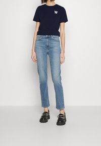 Navy modrá bavlněná trička s bílým logem na levé hrudi, spárovaná se světle modrými džíny. Černé silné boty dokončují celý outfit.