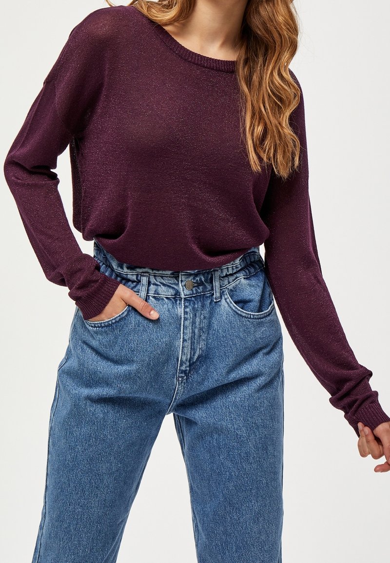 Pull long bordeaux à manches longues avec une coupe ample, associé à un jean en denim bleu taille haute. Texture douce, encolure arrondie et poignets côtelés.