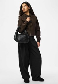 Veste marron courte zippée avec col, associée à un pantalon large noir. Accompagnée d'un sac à main tissé noir texturé.