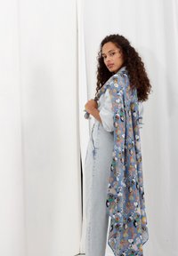 Écharpe bleu clair ornée de personnages de dessin animé avec une texture douce. Elle se drape élégamment et est portée sur une tenue en denim.