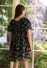 Svart blommig klänning med korta puffärmar, genomskinligt tyg, sammangal design och knytning i ryggen, med olika små blommönster.