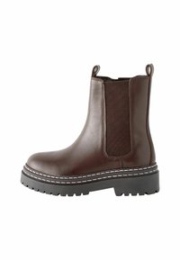 Brun läderankelboot med elastiska sidopaneler, kontrasterande vit söm och en texturerad svart gummisula.
