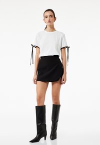 Witte kortemouwen T-shirt met zwarte lintstrikken, gecombineerd met een zwarte mini-rok met een zijsplitsing, en hoge zwarte puntige laarzen tot de knie.