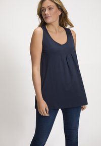 Top senza maniche di colore blu navy con scollatura a V e dettaglio plissettato nella parte anteriore, realizzato in un materiale morbido. Abbinato a jeans blu scuro.