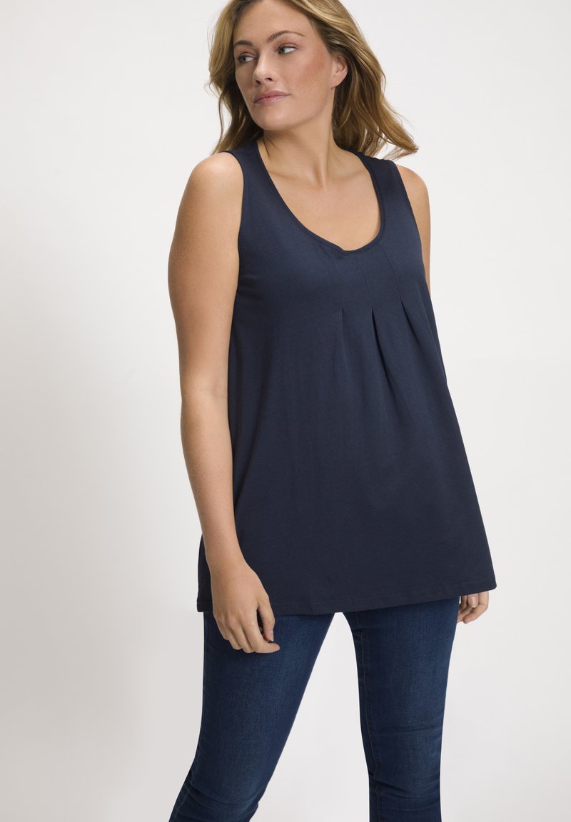 Top senza maniche di colore blu navy con scollatura a V e dettaglio plissettato nella parte anteriore, realizzato in un materiale morbido. Abbinato a jeans blu scuro.