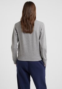 Grå sweatshirt med rund halsringning och ribbad mudd, matchad med mörkblå joggers. Tyget verkar mjukt och texturerat.