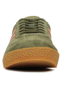Sneaker verde in suede con accenti arancioni, punta rotonda, suola in gomma testurizzata e design con lacci. Presenta un tallone rinforzato e un branding minimale.