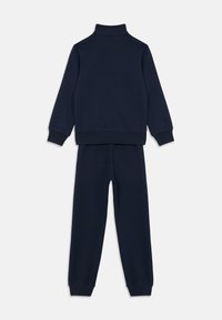Conjunto de sudadera de cuello alto de manga larga en azul marino y pantalones de chándal a juego con puños y dobladillo acanalados, mostrado en plano desde la parte trasera.