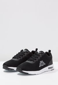 Svarta sportskor i mesh med texturerad yta, vita detaljer och logotyp. Har snörning och luftkuddar i sulan.