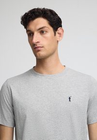 Grijze katoenen t-shirt met een ronde hals, voorzien van een kleine marineblauwe logoafdruk op de linkerborst. Korte mouwen en een zachte, gladde textuur.