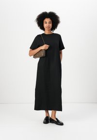 Black cotton midi dress with short sleeves and side slits, paired with a brown geometric handbag and black loafers. Simple, relaxed fit.