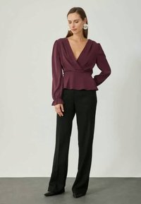 Haut enroulé bordeaux avec manches longues et taille peplum, associé à un pantalon noir à jambes larges. Tissu lisse avec un design structuré.