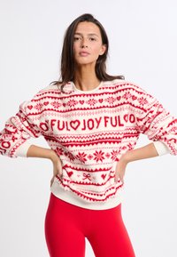 Czerwony i biały sweter z świątecznymi wzorami, w tym sercami, płatkami śniegu i napisem. Miękka, teksturowana tkanina o luźnym kroju i okrągłym dekolcie.