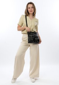 Zkrácený světle žlutý top z látky s knoflíky; kr�émové kalhoty s širokými nohavicemi; černá kožená crossbody taška se zipy; bílé tenisky.