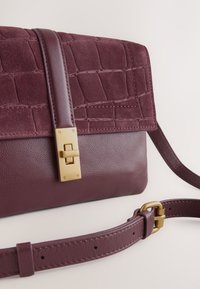 Burgundy bag in smooth leather with a croc-embossed flap. Features gold hardware and an adjustable strap, highlighting texture and design details.