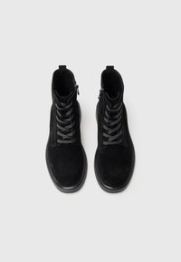 Black suede ankle boots with a rounded toe, flat sole, and gray laces. Features a side zipper for easy wear.