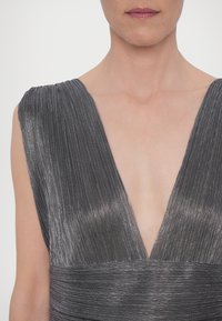 Abito da sera grigio metallico con scollatura a V profonda e texture plissettata. Presenta un tessuto liscio e luminoso con vita aderente e spalline larghe.